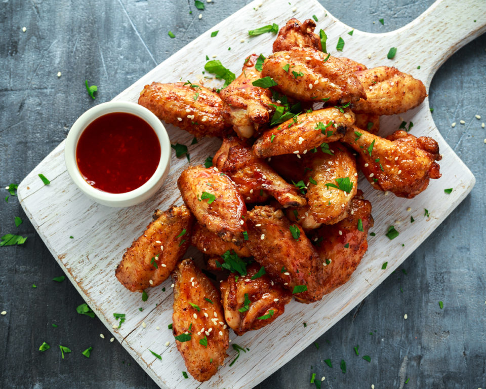 Baked chicken wings with sesame seeds and sweet chili sauce on white wooden board.