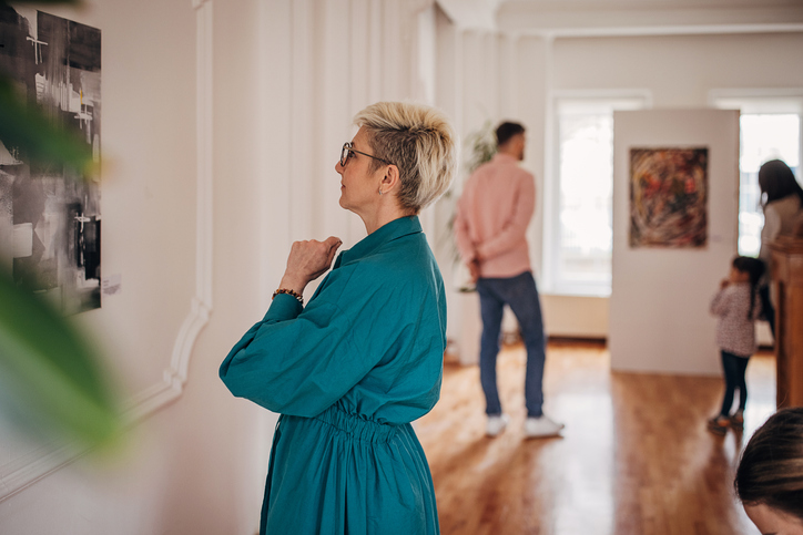 Diverse group of visitors in modern art gallery looking at paintings.