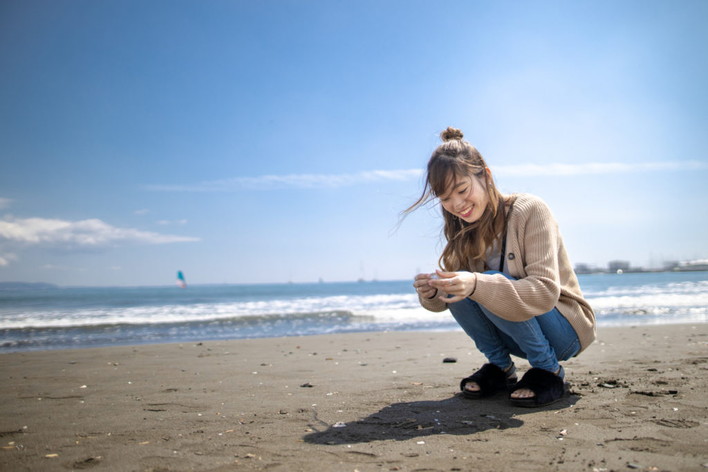 Young woman picking up sea shells on beach