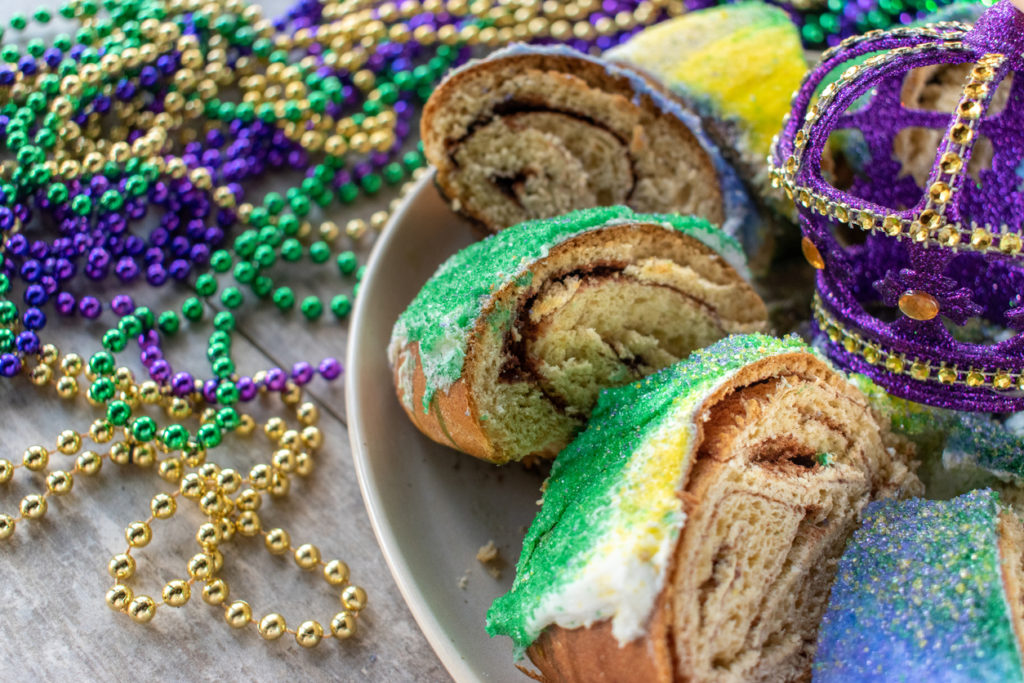 King cake on a large platter on a counter with gold, purple, and green mardi gras beads